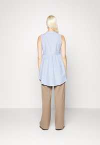 Top sem mangas listrado em algodão azul e branco com um peplum pregueado, combinado com calças largas bege. Decote simples e costas mais longas.