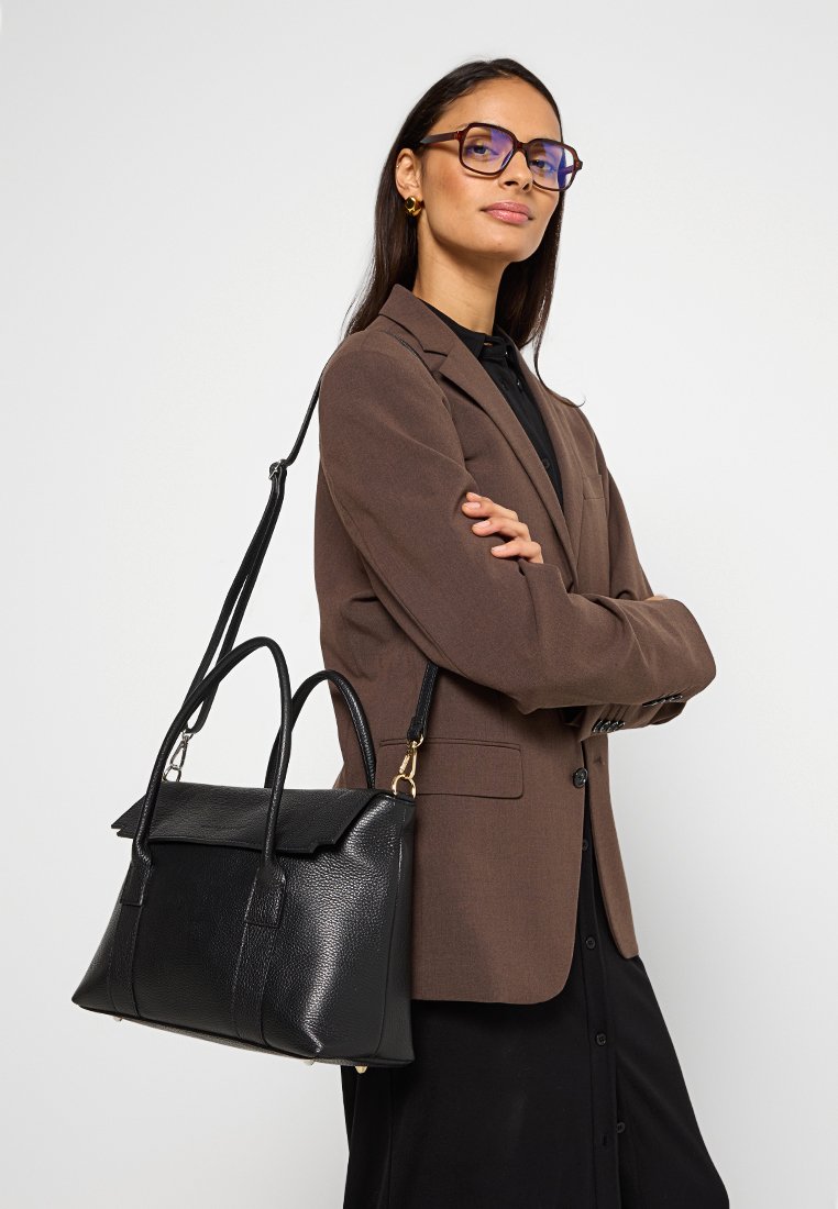 Sac à main en cuir noir avec une forme structurée et une texture lisse, doté de poignées supérieures doubles et d'une sangle réglable. Accents dorés visibles.