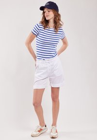 Blauwe en witte gestreepte shirt met korte mouwen, gecombineerd met witte shorts met een elastische tailleband en knopen. Gecombineerd met een marineblauwe pet en sneakers.