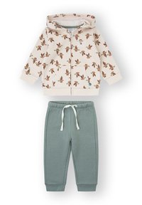 Sudadera con capucha y cremallera en color crema con estampado de pájaros, combinada con pantalones deportivos verdes que cuentan con cintura y puños elásticos.