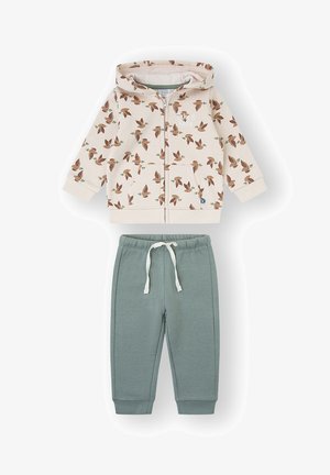 Sudadera con capucha y cremallera en color crema con estampado de pájaros, combinada con pantalones deportivos verdes que cuentan con cintura y puños elásticos.
