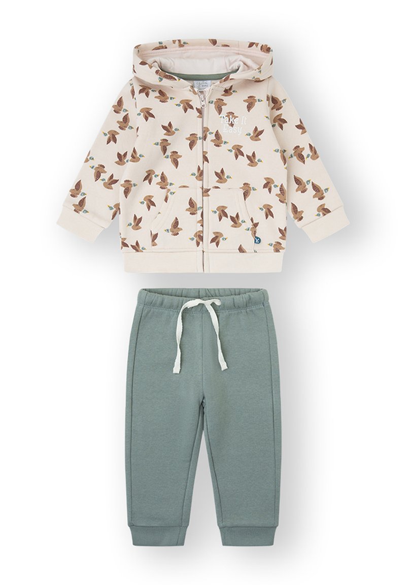 Sudadera con capucha y cremallera en color crema con estampado de pájaros, combinada con pantalones deportivos verdes que cuentan con cintura y puños elásticos.