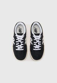 Sorte semskede sneakers med hvite snører, med perforert tå, hvit "N"-logo på siden, og en beige gummisåle.