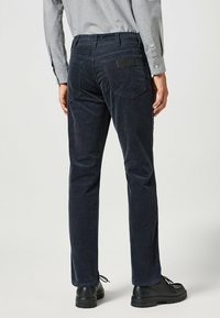 Pantalones de pana azul marino con corte recto, que cuentan con bolsillos delanteros, bolsillos de parche en la parte posterior y una etiqueta de la marca en la pretina.