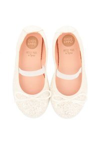 Bailarinas blancas con acabado brillante, cinta elástica y detalle de lazo en la punta. Forro interior de color rosa suave. Fabricadas en España.