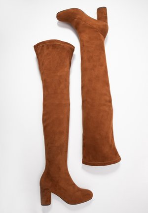 Brązowe zamszowe kozaki za kolano z zaokrąglonymi noskami i masywnymi wysokimi obcasami, ułożone płasko na białym tle.