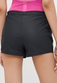 Shorts de sport noirs au tissu lisse et à la coupe ajustée, dotés d'une couture arrière élégante et d'un style minimaliste.