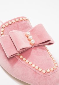 Mocassin en daim rose avec un grand nœud et des clous décoratifs en perles le long des bords et au centre du nœud.