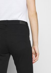 Jeans de mezclilla negros con un diseño ajustado, que cuentan con un detalle de costura en el bolsillo trasero y una etiqueta de cuero de la marca en la cinturilla.