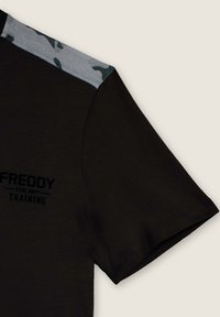 Maglietta sportiva nera a maniche corte, con un pannello sulle spalle a motivo mimetico grigio e testo nero che recita "FREDDY ATHL DEPT TRAINING."