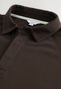 Dunkelbraunes Polo-Shirt aus strukturierter Stoffqualität mit Kragen, Knopfleiste und einem kleinen Logosticker am Hals.