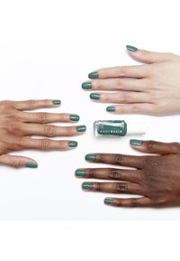 Lo smalto verde è applicato su più mani di diverse tonalità della pelle. La bottiglia di smalto è centrata, mettendo in mostra il suo design e l'etichetta.