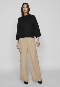 Jersey negro de gran tamaño con cuello redondo y mangas 3/4, combinado con pantalones cargo de pierna ancha beige, que cuentan con bolsillos laterales y un corte holgado.