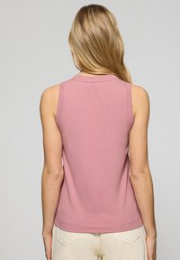 Bez rękawów, jasnoróżowa koszulka wykonana z bawełny, z okrągłym dekoltem i subtelnym wykończeniem. Gładka tekstura bez wzorów lub akcentów.