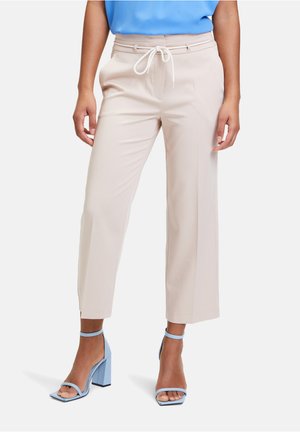 Pantalons beige coupés, avec une taille à cordon et des plis à l'avant. Associés à des sandales à talons bloc bleu clair. Tissu lisse et ajusté.