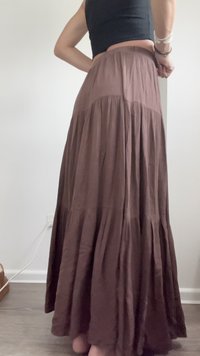 Jupe longue marron à plusieurs volants en tissu léger, dotée d'une taille haute et d'une silhouette fluide. Texture lisse avec un léger éclat.