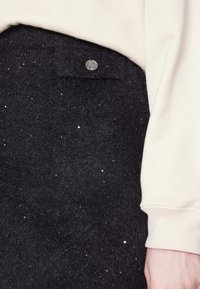 Jupe en feutre noir parsemée de paillettes argentées, avec une poche avant fermée par un bouton argenté, assortie à un sweat-shirt couleur crème.