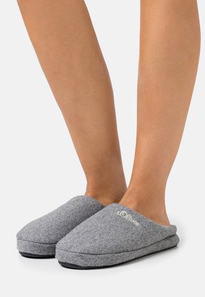 Chaussons gris en feutre avec un design de bout arrondi, une texture douce et un logo brodé subtil sur le dessus, dotés d'une semelle en caoutchouc noir.