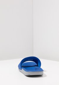 Blå sklidesandal med teksturert stroppe og fotseng, grå yttersåle med riller for grep. Jevn finish og åpne tådesign.