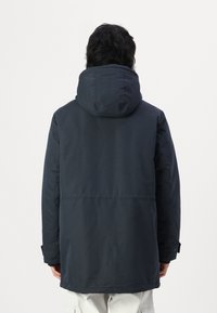 Chaqueta impermeable de color azul marino oscuro con una gran capucha, mangas largas y corte recto. Presenta costuras cosidas y puños ajustables.