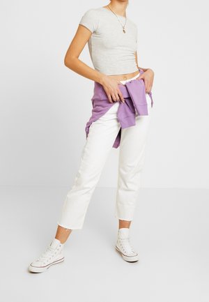 Mujer que lleva pantalones cortos blancos, zapatillas altas blancas, una camiseta gris corta y un sudadero morado atado alrededor de la cintura.