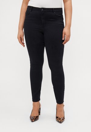 Juodos lieknos džinsinės kelnės iš elastingos denim medžiagos, su aukštu liemeniu, penkių kišenių dizainu ir tvarkingais siūlais. Dėvimos su smailiomis gyvūnų rašto aukštakulnėmis bateliais.