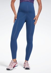 Leggings de cintura alta, justos ao corpo, em tecido azul escuro sólido. Textura suave com um acabamento brilhante. Combinados com sapatilhas de treino rosas.
