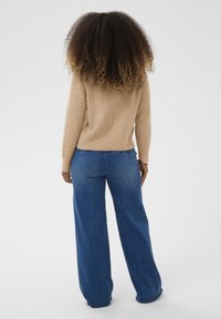 Bežs adīts džemperis ar brīvu piegulšanu, apvienots ar plašām zilo džinsu biksēm. Džemperim ir ribotas piedurknes un apakša, gluda tekstūra.