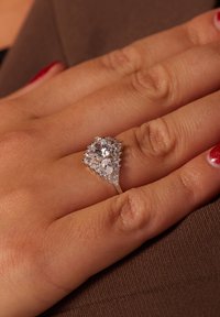 Zilveren ring met een driehoekig ontwerp, voorzien van een centrale heldere steen en kleinere peervormige accenten, allemaal omringd door sprankelende micro-pavé.