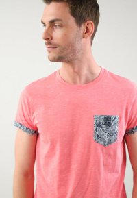 Camiseta de manga corta rosa con tejido texturizado, que presenta un bolsillo de contraste con un patrón y puños con estampado.