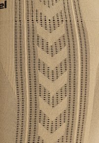 Beige stof met een gestructureerd patroon van zwarte chevrons en gestippelde lijnen. Glad breiwerk met duidelijke verticale ribbels en een subtiele glans.