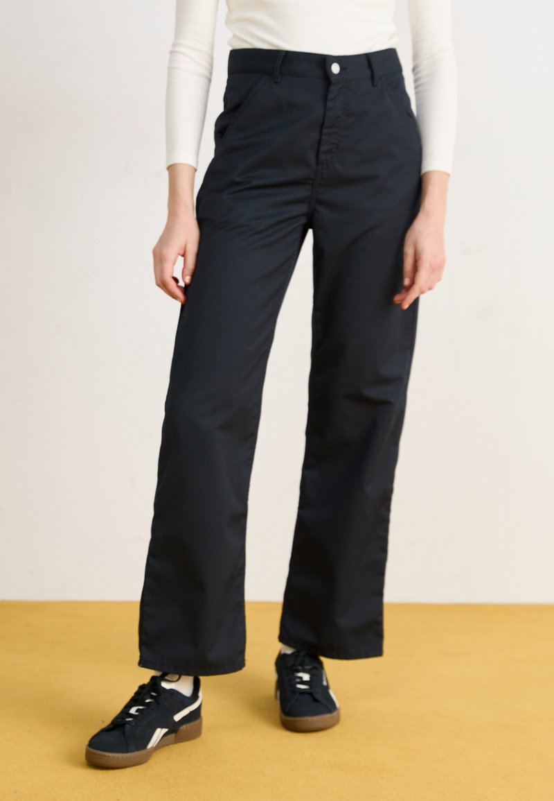 Black, loose-fitting trousers with a smooth texture, featuring a front button closure, side pockets, and worn with black sneakers.