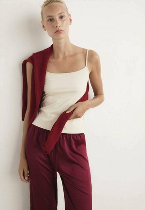 Top in cammello e pantaloni da pigiama bordeaux, con un maglione bordeaux poggiato sul braccio. Tessuto morbido, vestibilità comoda e design semplice.