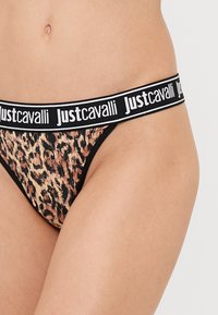 Tanga s leopardím vzorom s čiernym elastickým pásom s bielym logom "Just Cavalli". Mäkký materiál, minimalisticý dizajn, nízky strih.