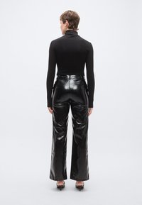 Fekete garbó felsőrész, amelyhez magas derekú, fényes fekete széles szárú nadrág van p�árosítva, hangsúlyozva a letisztult textúrát és strukturált sziluettet.