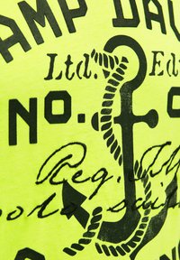 Gelbes Baumwoll-T-Shirt mit fett gedrucktem schwarzem Text und Anker-Design, mit Seil-Akzenten und Details in handgeschriebener Schrift.