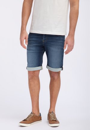 Shorts en denim bleu foncé, avec un design décoloré, des ourlets roulés et un style classique à cinq poches, associés à des baskets marron.