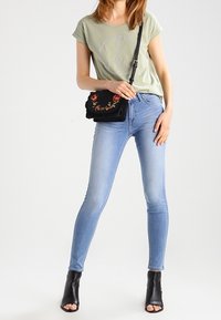 Světle zelené tričko s symbolem míru, spárované s modrými skinny džíny. Černá kabelka s květinovou výšivkou. Černé kotníkové boty na podpatku.