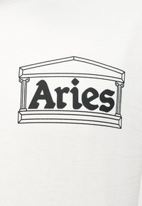 Μαύρο κείμενο "Κριός" περιβαλλόμενο από ένα απλό μαύρο σχέδιο γραμμής ενός κλασικού προστώου ναού σε λευκό υφασμάτινο φόντο.