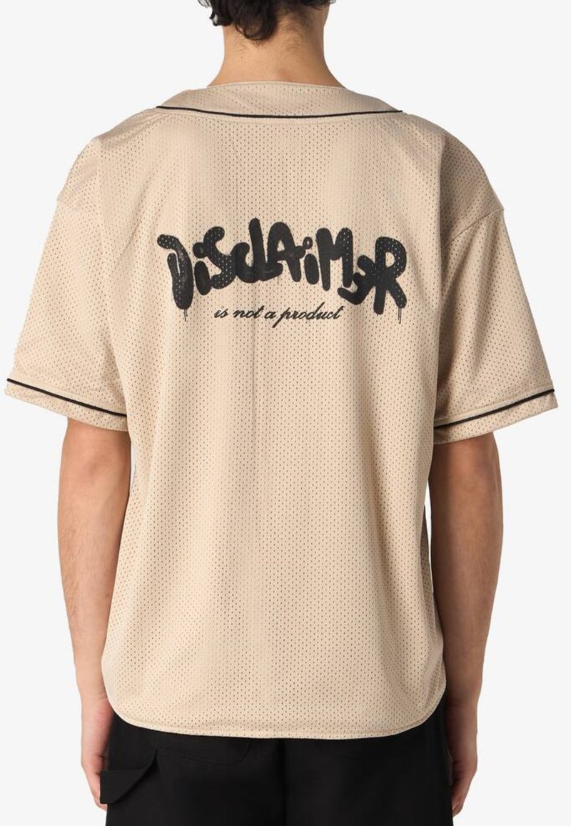 Camicia beige a maniche corte in rete con una vestibilità ampia. Presenta accenti neri e una scritta grafica sulla schiena che dice "La dichiarazione non è un prodotto."