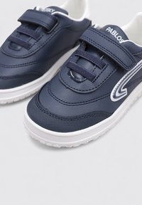 Baskets bleu marine avec une tige synthétique lisse, semelle en caoutchouc blanc, sangle Velcro réglable et lacets tissés pour un ajustement sécurisé.