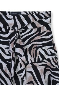 Schwarz-weißer, zebra gestreifter Stoff mit beigen Akzenten, featuring einen Knoten-Detail an der Taille und einer weichen, strukturierten Oberfläche. Größe S.