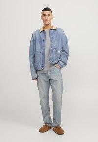Leren spijkerjasje in lichtblauw met een beige kraag, twee voorzakken, knoopsluiting, gecombineerd met een grijze T-shirt en lichtblauwe spijkerbroek. Bruine instappers.