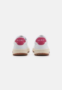 White sneakers with pink accent heel, textured outsole, and speckled cream midsole. Simple design, lace-up closure, and rounded toe.
