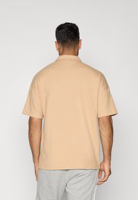 Korte mouwen polo in lichtbeige met een gestructureerd patroon, voorzien van een puntkraag en een relaxte pasvorm, gecombineerd met grijze sweatpants.
