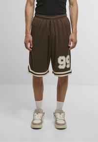 Shorts de sport marron avec des accents blancs et un grand imprimé '99', dotés d'une taille élastique et d'une coupe décontractée. Associés à des baskets claires.