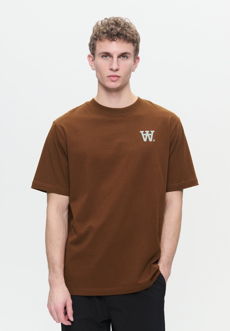 Brown cotton t-shirt with a round neckline, short sleeves, and a small white logo on the left chest. Smooth texture and relaxed fit.