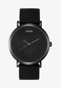 Reloj con correa de silicona negra y esfera redonda negra que presenta un patrón de panal triangular, agujas de horas y minutos plateadas, y el nombre de la marca "GUESS."