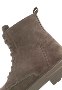 Botín de ante gris hasta el tobillo con diseño de cordones, talón reforzado y suela de goma texturizada con ranuras horizontales.