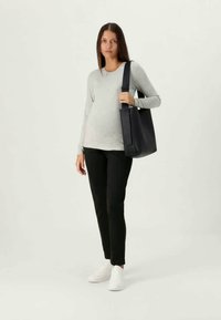 Svart tote-veske med glatt finish, med en bred stropp og minimalistisk design. Modellen har på seg en lysegrå langermet skjorte og svarte bukser.